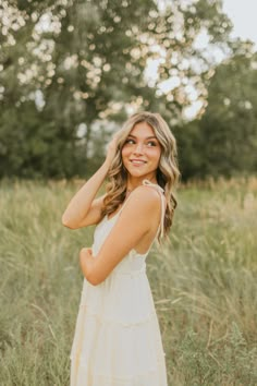 a woman standing in tall grass with her hand on her head and smiling at the camera