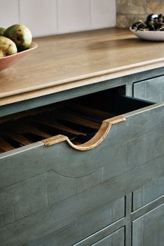 a bowl of fruit sitting on top of a wooden counter next to an open drawer