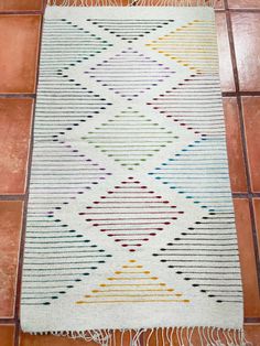 a white rug with multicolored stripes and fringes on top of a tile floor