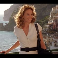 a woman standing on top of a balcony next to the ocean with buildings in the background