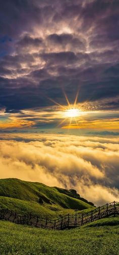 the sun shines brightly in the clouds above a grassy hill with a wooden fence