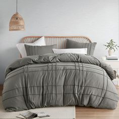 a bed with grey comforter and pillows in a room next to a lamp on the wall