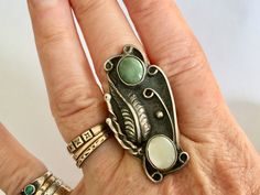 "an amazing and amazingly tall southwestern ring, artisan-made. top stone looks like a green turquoise, bottom one is a mother-of-pearl. beautiful feather and details, nice condition. marked with a stamping on the back. has a fair amount of patina but not much in the way of wear. mother-of-pearl shows some surface wear. size: 5.75 height of face: 1 and 15/16\" width of face: a bit over 13/16\" width of inner band: a bit over 1/16\"" Bohemian Multi-stone Opal Ring, Green Bohemian Jewelry With Inlay, Bohemian Green Jewelry With Inlay, Bohemian Green Inlay Jewelry, Collectible Green Turquoise Bohemian Ring, Collectible Bohemian Green Turquoise Ring, Green Bohemian Multi-stone Rings, Bohemian Green Multi-stone Rings, Bohemian Green Turquoise Collectible Ring