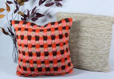 two knitted pillows sitting next to each other on a white surface with plants in the background