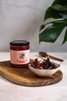 a jar of jam sitting on top of a wooden cutting board next to a bowl of dried cranberries