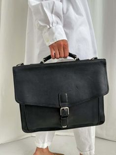 Vintage unisex charbon et argent coach leather briefcase    - striking all black tone with cool silvery metal details    - smooth and thick leather construction  - adjustable buckle closure  - classic inner coach stamp  - numerous inner compartments and wallet  - hand crafted quality    height: 12 in.  width: 15 in.  base depth: 2 1/4 in.    pair with our stunning selection of vintage dresses.    although we do our best to ensure each item is in excellent condition please respect any minor flaws due to the item's vintage character. People Holding Hands, Luxury Leather Bag, Vintage Character, Leather Briefcase, Coach Leather, Vintage Coach, All Black, Vintage Dresses, Leather Bag