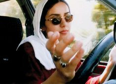 a woman wearing sunglasses sitting in the driver's seat of a car while holding her hand out