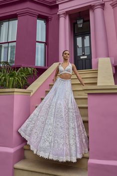 a woman in a white and pink dress standing on some steps with her arms behind her back