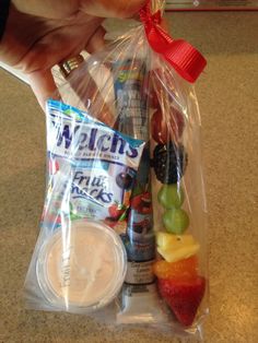 a person is holding a plastic bag full of fruit and snacks on the counter top