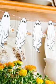 a bunch of ghost decorations hanging from a kitchen shelf with flowers in the foreground