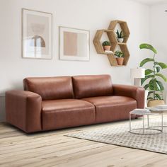 a brown leather couch sitting in a living room next to a coffee table and potted plants