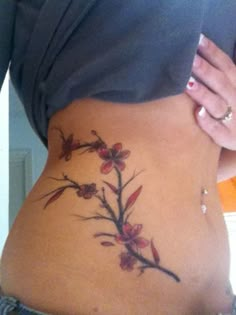 a woman's stomach with a tattoo on the side that has red flowers growing out of it