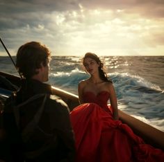 a woman in a red dress sitting on a boat with a man looking at her