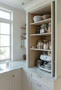 an open cabinet in the corner of a kitchen with lots of jars and containers on it