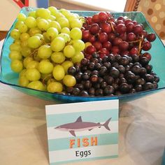 a bowl filled with grapes and other fruit on top of a table next to a sign that says fish eggs