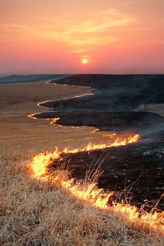 a fire hydrant on the side of a dry grass field at sunset with bright flames coming from it