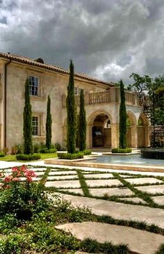 a large stone building with trees and flowers in the foreground, on a cloudy day