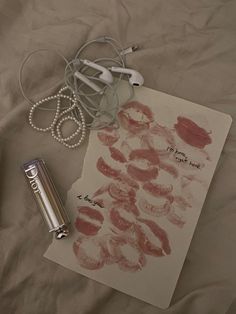 an open notebook with lipstick on it next to headphones and earbud plugs