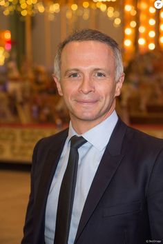 a man in a suit and tie smiling for the camera at an amusement park with lights behind him