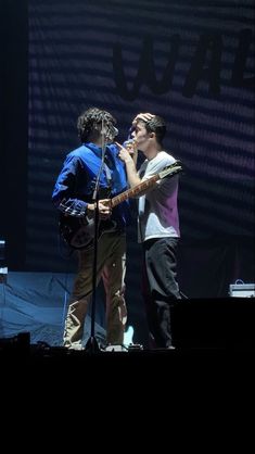 two young men singing into microphones on stage