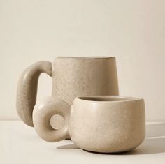 two coffee mugs sitting next to each other on a white tableclothed surface