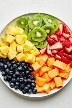 a white plate topped with fruit and kiwis on top of blueberries next to strawberries