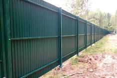 a green metal fence next to a dirt field