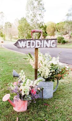 a sign that says wedding on it sitting in the grass next to flowers and watering can