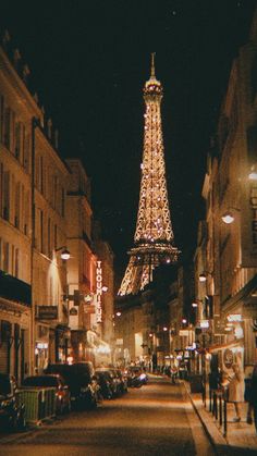 the eiffel tower lit up at night with people walking down the street below