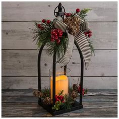 a candle is sitting in a lantern with holly and pine cones on it, decorated with a bow