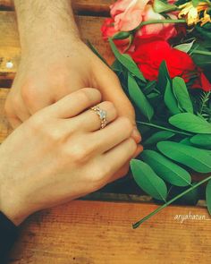 two people holding hands with flowers and greenery in the background, close up on their wedding rings