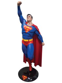 a statue of a man dressed as superman with his hand up in the air and wearing a red cape