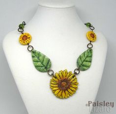 A golden yellow sunflower in full bloom sits at the center of this boho statement necklace surrounded by lush green leaves. The hand painted polymer clay sunflower and leaves are connected to smaller sunflower beads and Czech glass accents.  The rustic style of this necklace is enhanced by the rich browns of patinated brass chain. The sunflower focal is about 2 inches (5 cm) diameter.  The necklace is adjustable from 16 inches (40 cm) to 18 inches (46 cm) length and fastens with a large lobster clasp. For more original necklace creations from Paisley Lizard Designs, see this section of my shop https://www.etsy.com/shop/PaisleyLizardDesigns?section_id=5828774 Find more sunflower jewelry in my shop - https://www.etsy.com/shop/PaisleyLizardDesigns?search_query=sunflower Jewelry care: I do not Hand Painted Yellow Polymer Clay Jewelry, Hand-painted Yellow Polymer Clay Jewelry, Yellow Bohemian Jewelry With Sunflower Design, Bohemian Yellow Jewelry With Sunflower Design, Bohemian Yellow Sunflower Design Jewelry, Polymer Clay Sunflower, Sunflower Beads, Clay Sunflower, Boho Sunflower