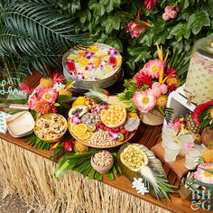 an assortment of food on a table with flowers and palm fronds around it