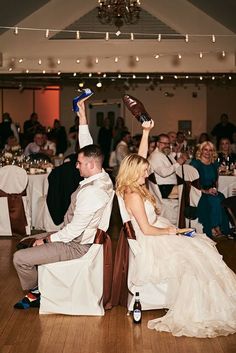 a man and woman sitting on chairs at a table with their arms in the air