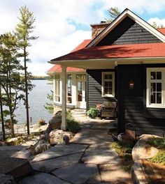 a black house with a red roof next to the water