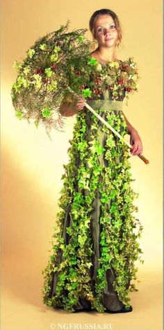 a woman in a green dress is holding a stick and flowers on her head while posing for the camera