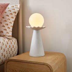 a white table lamp sitting on top of a wooden night stand