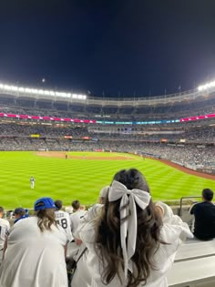 two women sitting in the stands at a baseball game looking out into the field with their backs to the camera