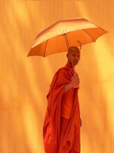 a man in an orange robe is holding an umbrella