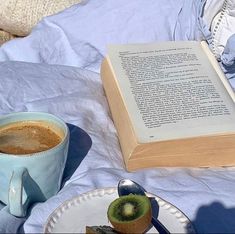 an open book sitting on top of a table next to a cup of coffee and kiwi