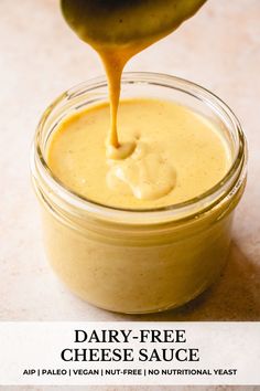 dairy - free cheese sauce in a glass jar being drizzled with a spoon