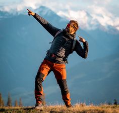 a man standing on top of a grass covered hillside pointing to the sky with his finger