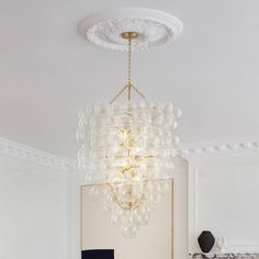 a chandelier hanging from the ceiling in a living room with white walls and furniture