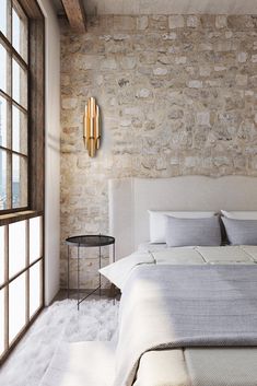 a bedroom with a stone wall and white bedding, along with a large window