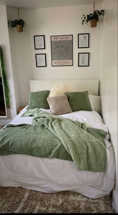 a bed with green blankets and pillows in a room next to pictures on the wall