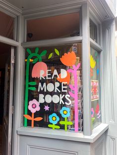 a store front window decorated with colorful paper flowers and leaves that reads read more books