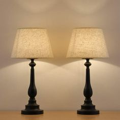 two lamps sitting on top of a wooden table next to each other with a white wall in the background