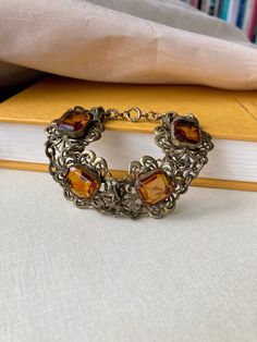 "Beautiful antique Art Deco era bracelet. Circa 1920s - 1930s or so.  Rich warm deep yellow-orange citrine-like glass faceted stones - so perfect for the rich Autumn colors of Fall. Fancy scroll links with etched designs on the connecting links. What a neat detail! Very Czech-looking although I didn't see any markings. Likely brass metal as most of these types of bracelets were during this time. In very good used antique condition. Light surface wear and normal aged tarnish and patina. Rich dark Vintage Amber Bangle Bracelet, Antique Citrine Gold Jewelry, Antique Gold Citrine Jewelry, Vintage Orange Metal Jewelry, Collectible Vintage Amber Jewelry, Antique Orange Gemstone Jewelry, Antique Gold Vintage Jewelry For Formal Occasions, Vintage Antique Gold Jewelry For Formal Occasions, Vintage Filigree Bracelet Collectible