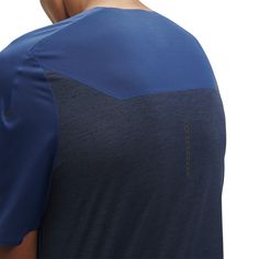 the back of a man's blue and black t - shirt, with his left hand on his hip